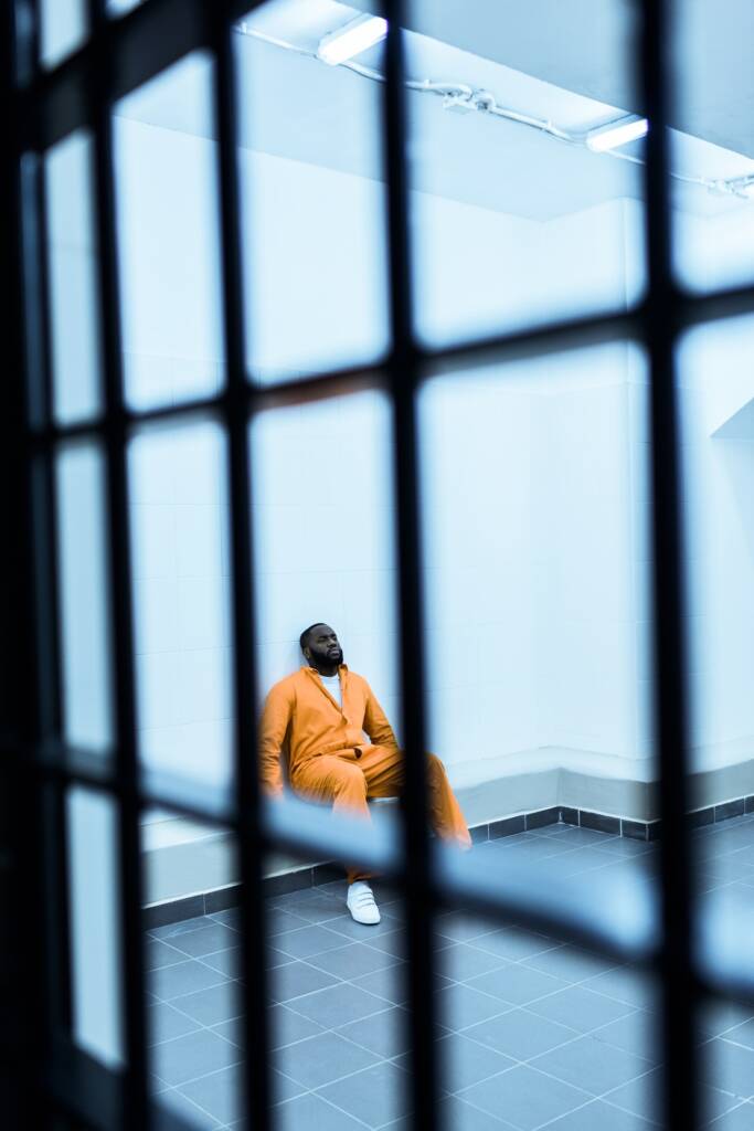 african american prisoner sitting on bench in prison cell